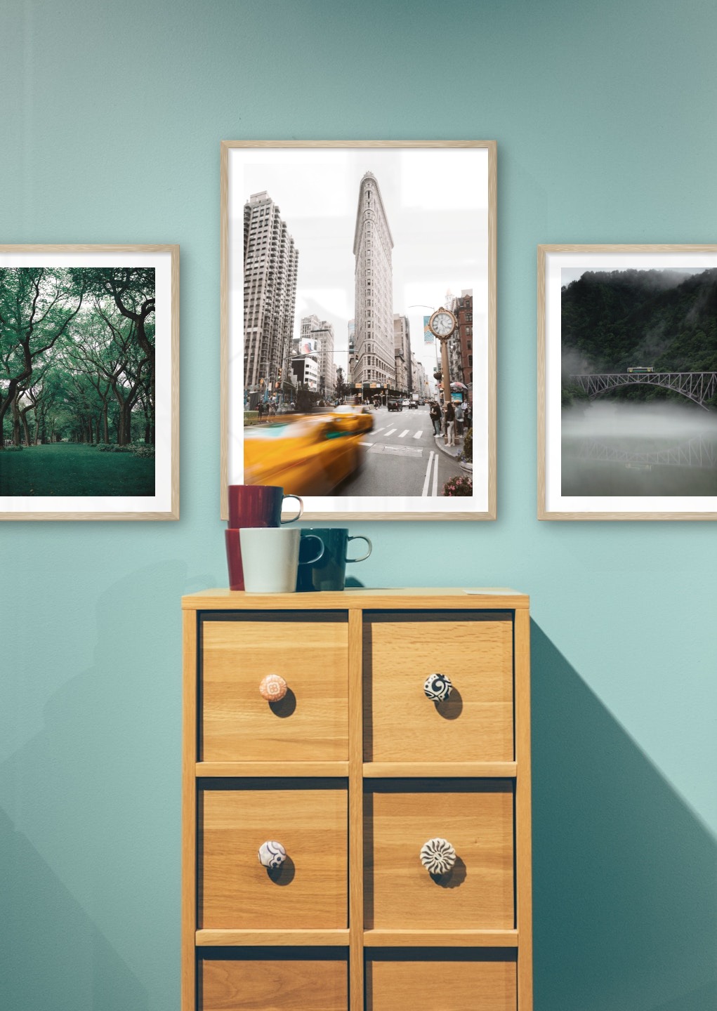 Gallery wall with picture frames in wood in sizes 40x50 and 50x70 with prints "Greenery and trees", "Yellow taxis in town" and "Train over bridge"