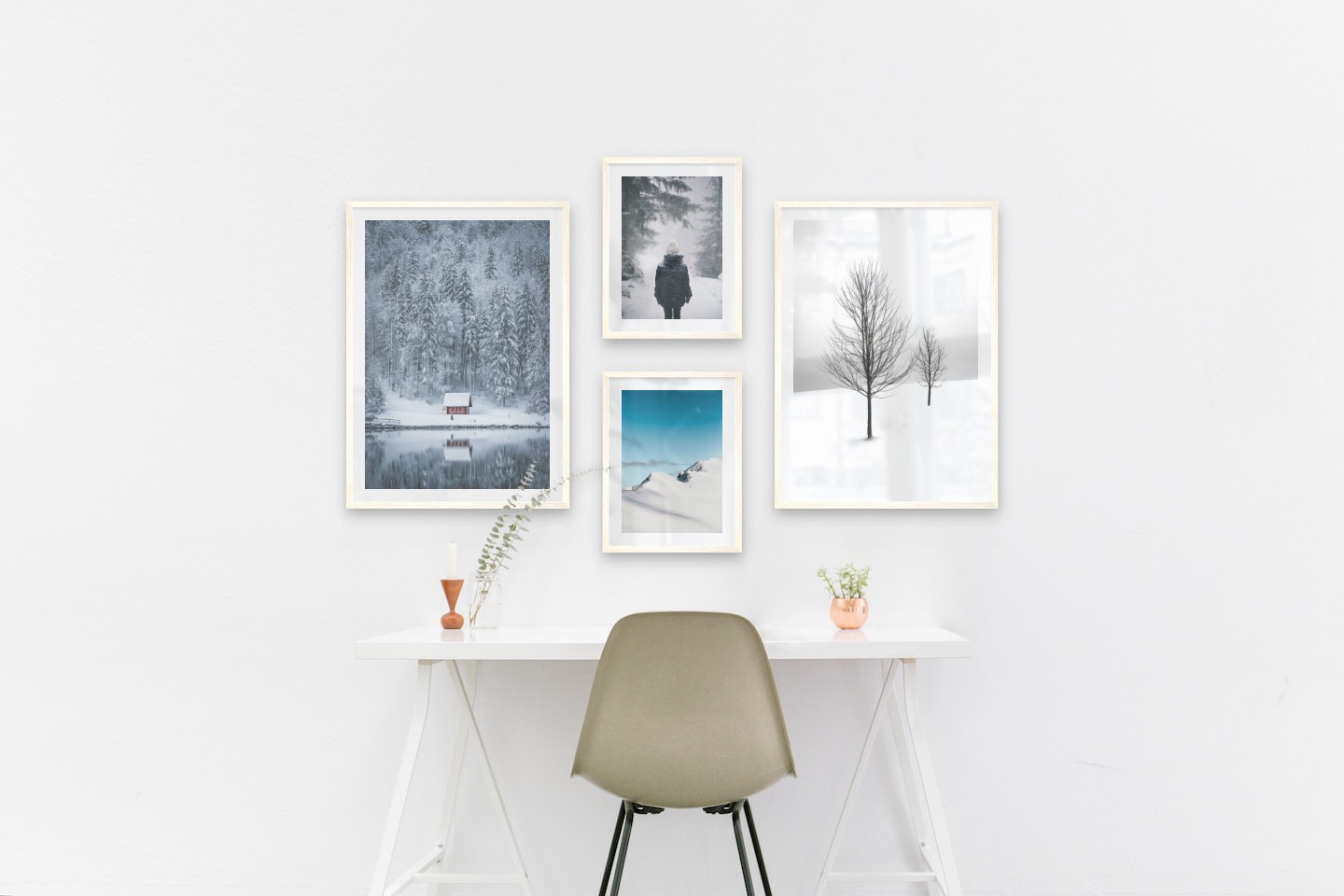 Gallery wall with picture frames in light wood in sizes 50x70 and 30x40 with prints "Cottage by the lake", "Person in the snow", "Snowy mountain peaks" and "Trees in the snow"