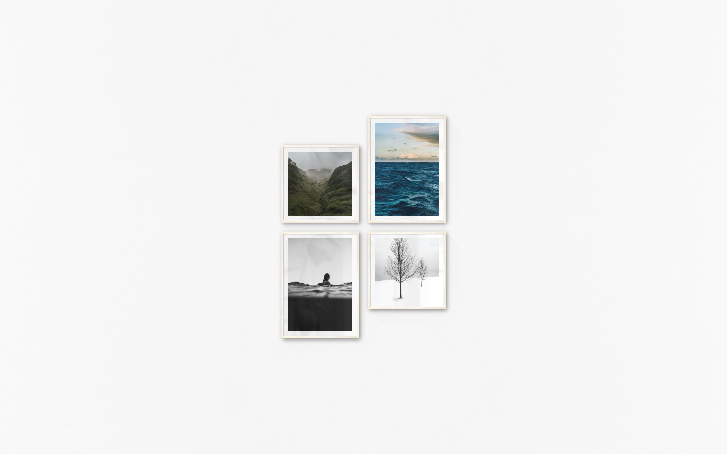 Gallery wall with picture frames in light wood in sizes 50x50 and 50x70 with prints "Stream in valley", "Somewhat out at sea", "Person in the water" and "Trees in the snow"
