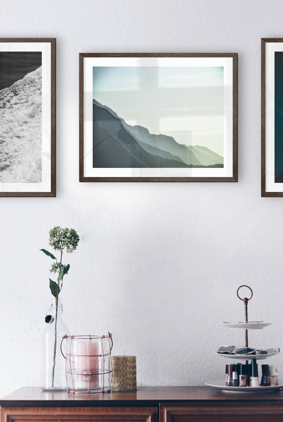 Gallery wall with picture frames in dark wood in sizes 50x50 and 40x50 with prints "Swell from waves", "Foggy mountain" and "Jar in front of space"