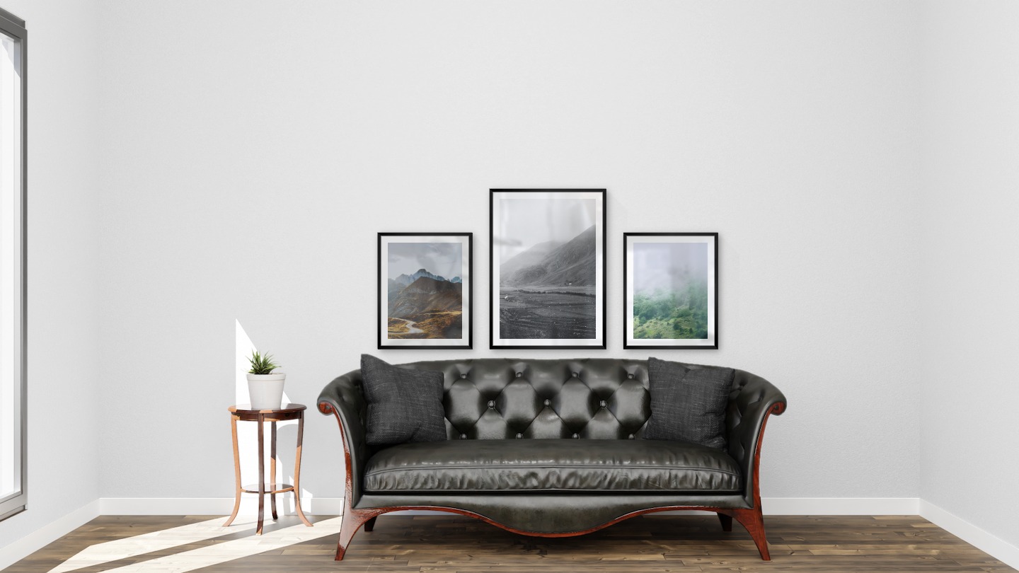 Gallery wall with picture frames in black in sizes 40x50 and 50x70 with prints "Road among the mountains", "Fields in front of mountains" and "Slope with trees"