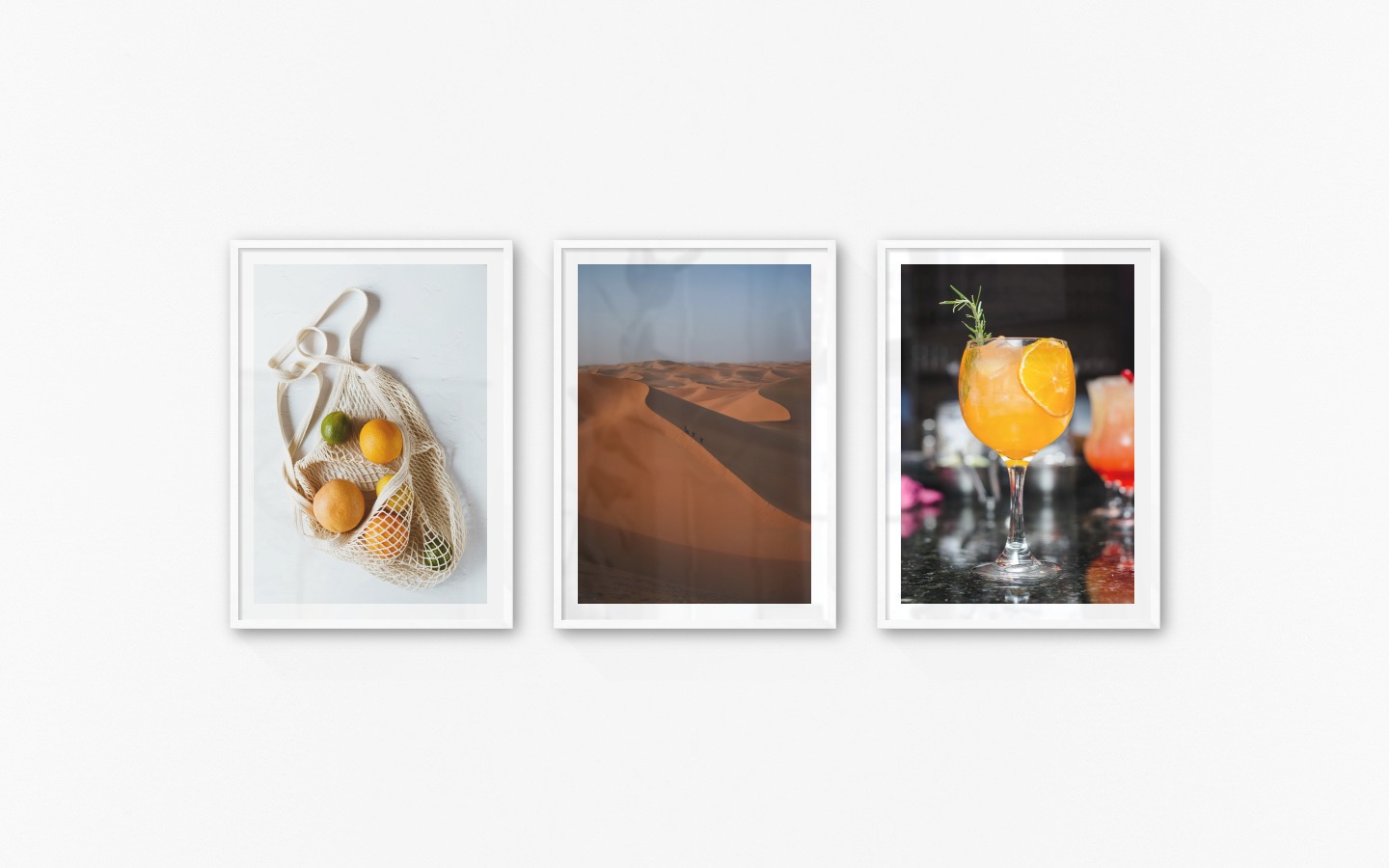 Gallery wall with picture frames in white in sizes 50x70 with prints "Fruit in a bag", "Desert" and "High orange drink"