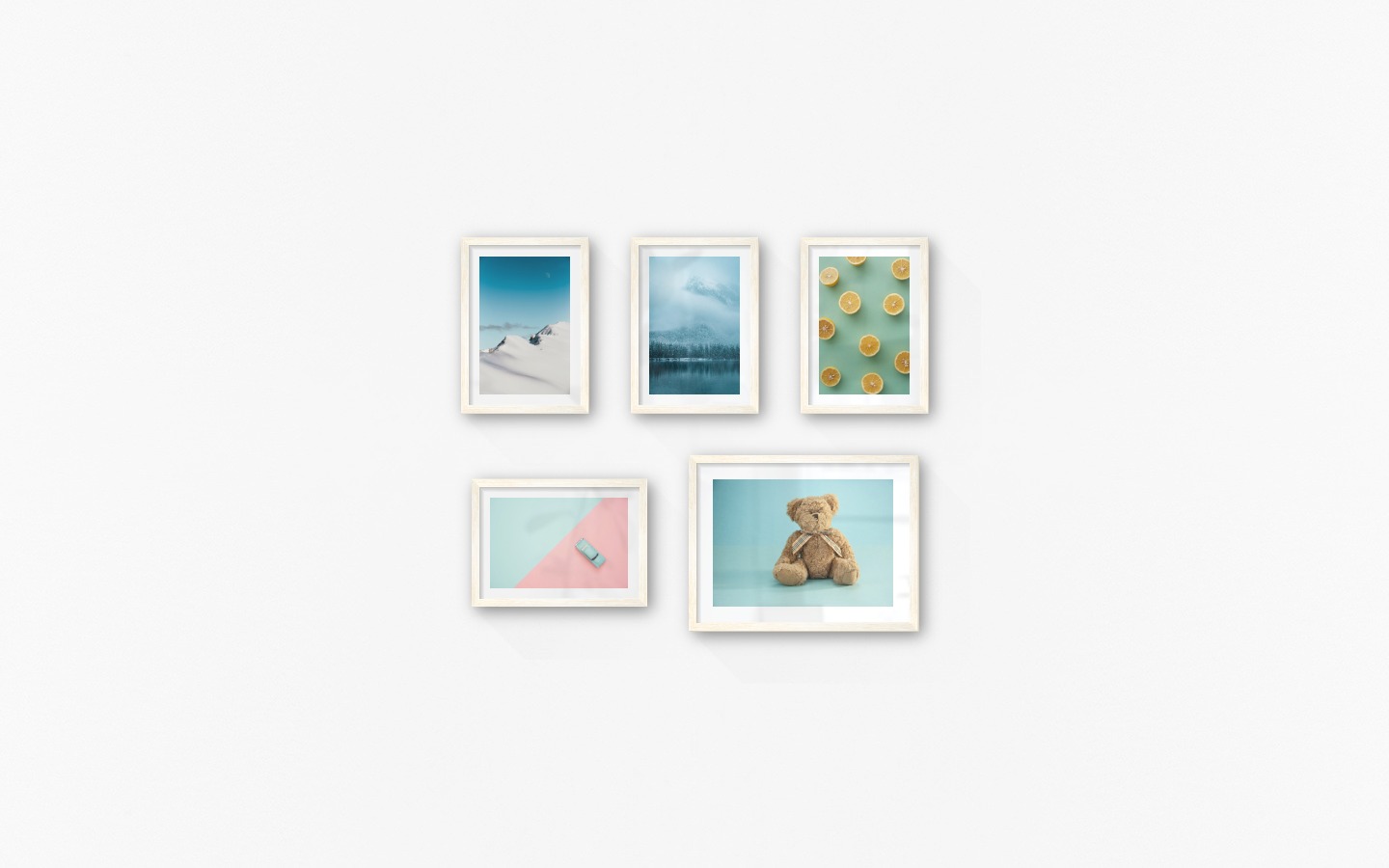 Gallery wall with picture frames in light wood in sizes 21x30 and 30x40 with prints "Snowy mountain peaks", "Lake, mountains and forest", "Lemons", "Blue car and pink" and "Teddy bear and blue"