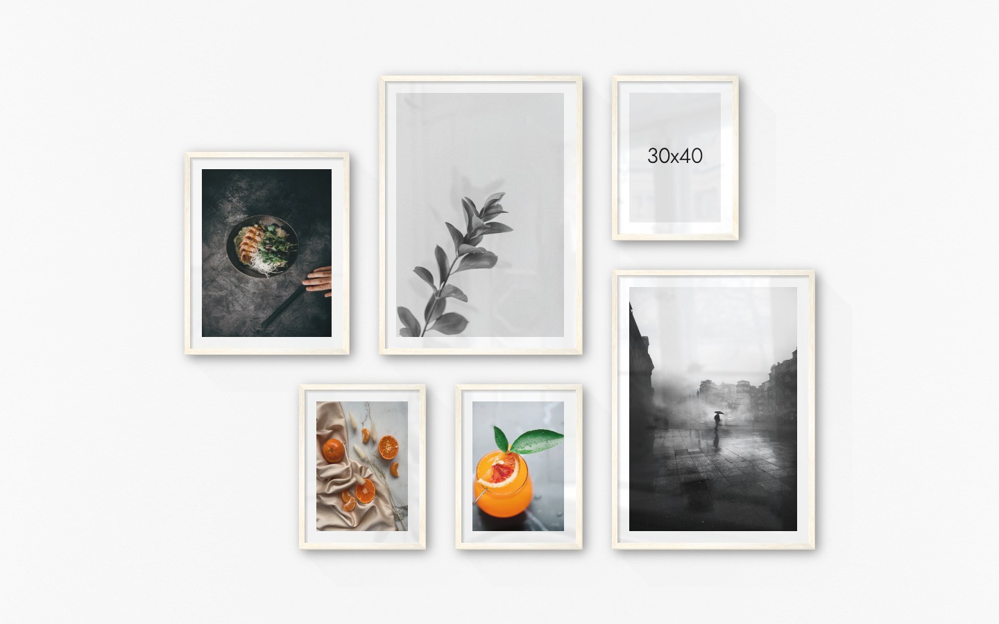 Gallery wall with picture frames in light wood in sizes 40x50, 50x70 and 30x40 with prints "Bowl", "Twig", "Oranges", "Orange drink" and "Rainy city"